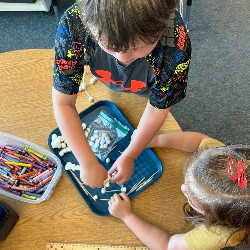 Two students work on putting toothpicks in marshmallows.